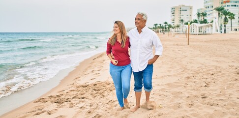 Wall Mural - Middle age hispanic couple smiling happy walking at the beach.