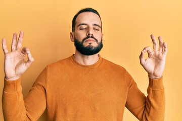 Young man with beard wearing casual winter sweater relax and smiling with eyes closed doing meditation gesture with fingers. yoga concept.