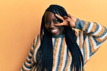 Sticker - Young black woman with braids wearing casual winter sweater doing peace symbol with fingers over face, smiling cheerful showing victory