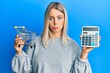 © Krakenimages.com - Beautiful blonde woman holding small supermarket shopping cart and calculator depressed and worry for distress, crying angry and afraid. sad expression.