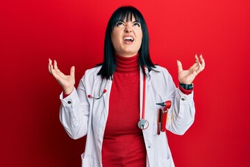 Poster - Young hispanic woman wearing doctor uniform and stethoscope crazy and mad shouting and yelling with aggressive expression and arms raised. frustration concept.