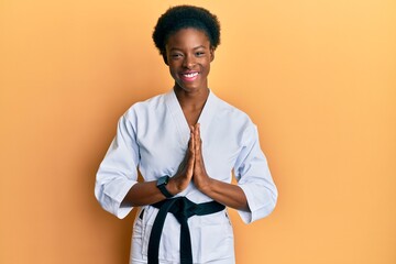 Canvas Print - Young african american girl wearing karate kimono and black belt praying with hands together asking for forgiveness smiling confident.