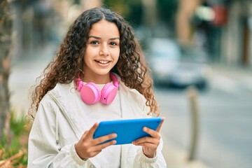 Wall Mural - Hispanic child girl smiling happy using headphones and touchpad at the city.