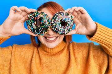 Sticker - Beautiful redhead woman holding tasty colorful doughnuts on eyes smiling with a happy and cool smile on face. showing teeth.