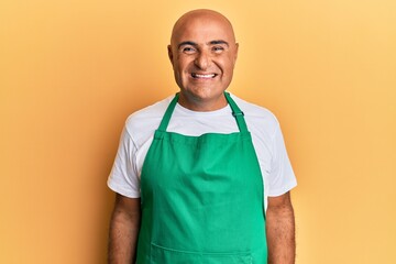 Mature middle east man wearing cleaner apron and gloves looking positive and happy standing and smiling with a confident smile showing teeth