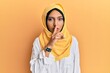 © Krakenimages.com - Young brunette arab woman wearing traditional islamic hijab scarf asking to be quiet with finger on lips. silence and secret concept.