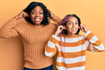 Poster - Beautiful african american mother and daughter wearing wool winter sweater smiling pulling ears with fingers, funny gesture. audition problem