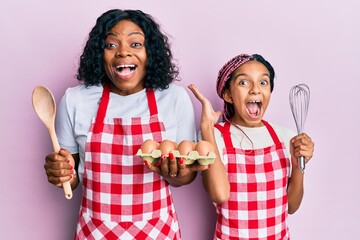 Sticker - Beautiful african american mother and daughter cooking cake using baker whisk celebrating crazy and amazed for success with open eyes screaming excited.