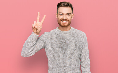 Young redhead man wearing casual winter sweater showing and pointing up with fingers number two while smiling confident and happy.