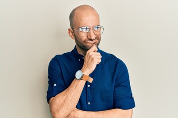 Wall Mural - Young hispanic man wearing casual clothes and glasses serious face thinking about question with hand on chin, thoughtful about confusing idea