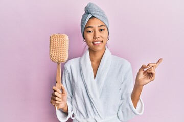 Sticker - Young chinese woman wearing shower towel cap and bathrobe holding sponge smiling happy pointing with hand and finger to the side