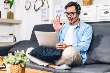 Wall Mural - Young smiling asian man using laptop computer working and video conference online meeting with colleagues at home.Young creative man talk video call with business team.work from home concept