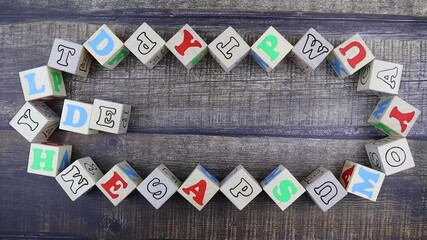 Fototapete - Word - Decoration - in colorful alphabet letters on wooden cubes surrounded by a frame of additional random blocks over a textured textile background. Stop motion, top view