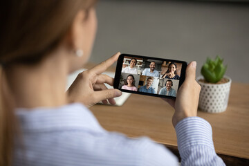 Close up back view of woman have webcam online team meeting with diverse colleagues on smartphone. Female talk speak on video call with multiracial businesspeople on cellphone. Virtual event concept.