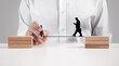 © Cagkan - Male hand draws a line between the wooden blocks for a businessman silhouette to walk across.