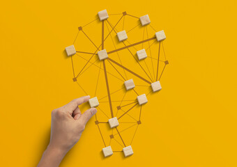 Business strategy, business management or business success concept. Hand is arranging wooden blocks in low polygon light bulb shape network on yellow background.