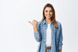 © Cookie Studio - Confident young woman with assured smile pointing left at copy space logo, showing good deal, recommending product, white background