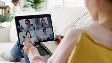 Wall Mural - Back view of business woman talking about sale report in video conference. Asian team using laptop and tablet online meeting in video call.Working from home, Working remotely and Social isolation.