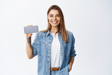 Portrait of young woman in casual clothes holding smartphone horizontal, showing empty mobile phone screen for app advertisement, white background