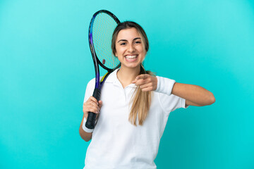 Young woman tennis player isolated on blue background surprised and pointing front