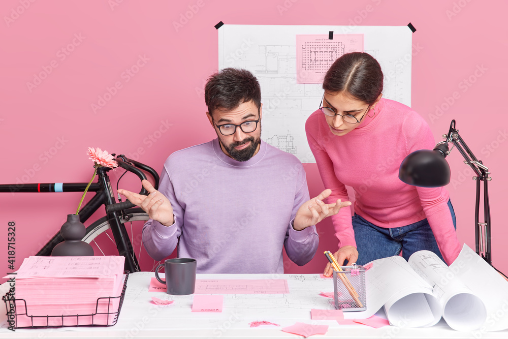 Puzzled man spreads hands looks confusingly at papers his female ...