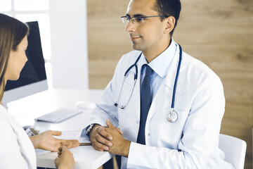 Doctor and patient discussing something while sitting at the desk in clinic. Concept of medicine and comfortable service in clinic