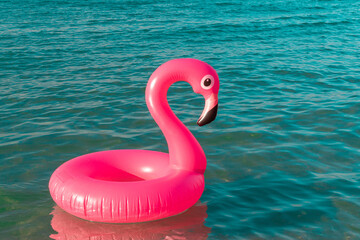 Summer holiday poster. Pink inflatable flamingo in blue ocean water for sea summer beach background. Funny bird toy for kids.