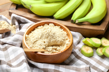 Bowl with banana flour on wooden background