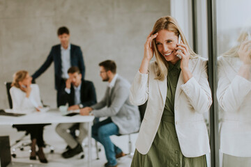 Wall Mural - Young business woman standing in the office and using mobile phone in front of her team