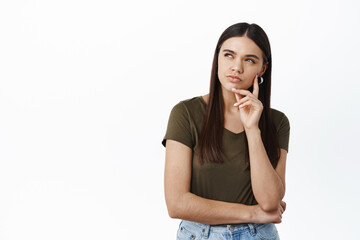 Wall Mural - Young thoughtful woman looking at upper left corner with squinting serious face, need to think, making assumption, standing pensive against white background