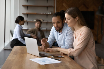 Canvas Print - African American businessman training intern, new employee, pointing at laptop screen, helping with corporate software, giving instructions, diverse colleagues working on online project together