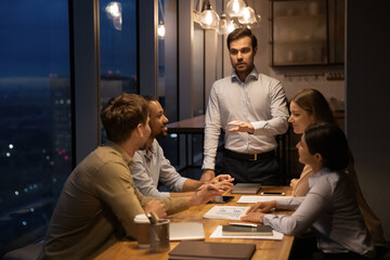 Poster - Confident businessman leading late corporate meeting with diverse employees, speaking, explaining marketing plan or project strategy, multiethnic colleagues listening to coach mentor at briefing