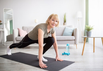 Wall Mural - Positive athletic senior woman doing runner's lunge yoga pose on home workout, copy space