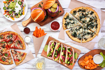 Wall Mural - Healthy plant based fast food table scene. Above view on a white wood background. Cauliflower crust pizzas, bean burgers, mushroom tacos, pepper nachos and cauliflower wings and sweet potato fries.