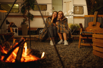 Wall Mural - girlfriends wrapped in plaid sitting by campfire