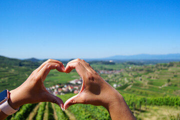 Close-up of a woman's hands forming a heart around a beautiful village surrounded by vineyards at Kaiserstuhl, Germany.