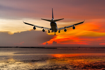 Wall Mural - rear view commercial passenger aircraft or cargo transportation airplane fly over coast of sea after takeoff from airport in evening with red sky