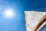 Fototapeta  - White sail against blue sky and sun