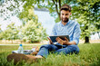 © baranq - Handsome young businessman sitting outdoors in the park and using tablet