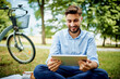 © baranq - Young businessman sitting on grass in park with tablet and bicycle