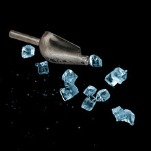 Flying Metal Ice Scoop And Blue Ice Cubes With Water Drops On Black Background