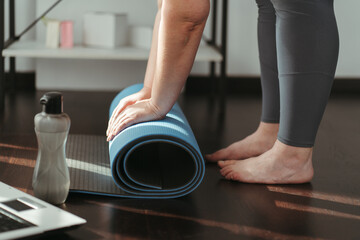 Active lifestyle, yoga trainer, flexibility, sport, fitness. Hands of young woman rolling yoga mat before workout with online trainer