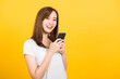 © sorapop - Asian happy portrait beautiful cute young woman teen smiling standing wear t-shirt using smart mobile phone looking to camera isolated, studio shot on yellow background with copy space