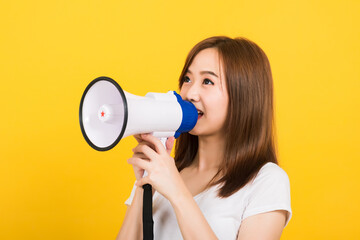 Asian happy portrait beautiful cute young woman teen standing making announcement message shouting screaming in megaphone looking to side isolated, studio shot on yellow background with copy space