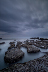 Wall Mural - Dreamy seascape for background. Beach with rocks and stones. Low tide. Blurred foggy water. Cloudy sky. Slow shutter speed. Soft focus. Copy space. Mengening beach, Bali