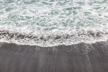 Wall Mural - Waterscape background. Black sand beach with white milky foam waves. Nature and environment concept. Black and white contrast. Daylight. Copy space. Volcanic beach in Bali