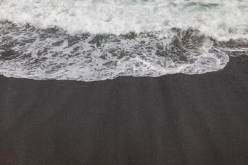 Wall Mural - Waterscape background. Black sand beach with white milky foam waves. Nature and environment concept. Black and white contrast. Daylight. Copy space. Volcanic beach in Bali