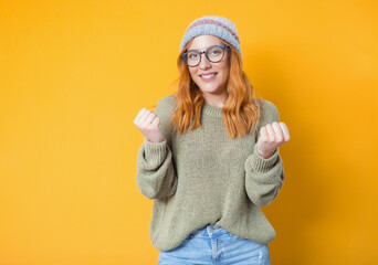 Excited young woman with clenched fists, isolated on yellow background. Yes concept. Good news. Rejoicing female celebrates success