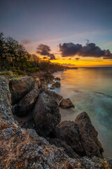 Wall Mural - Sunset view. Seascape background. Amazing ocean view. Beach with rocks and stones. Bright sunlight on horizon line. Cloudy sky. Vertical layout. Bali.