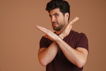 Wall Mural - Displeased unshaven young man showing stop gesture at camera